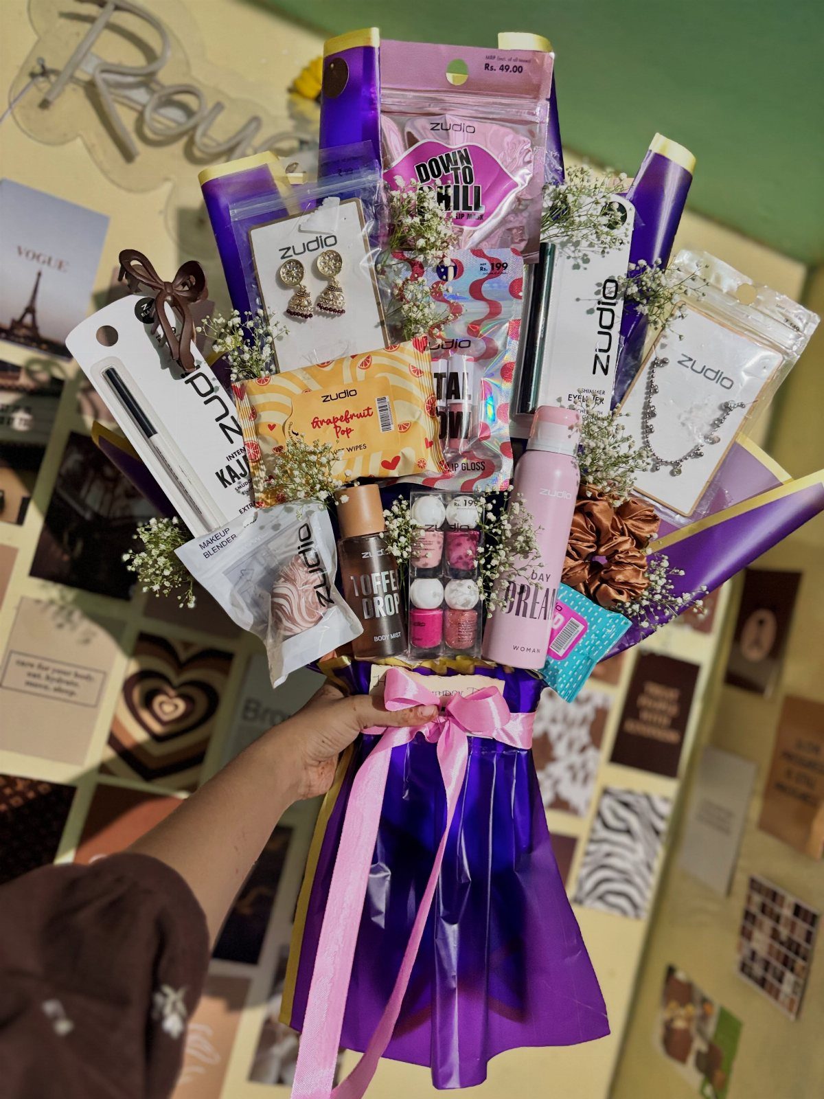 Gift bouquet with jewelry and beauty products wrapped in purple cellophane and pink ribbon.