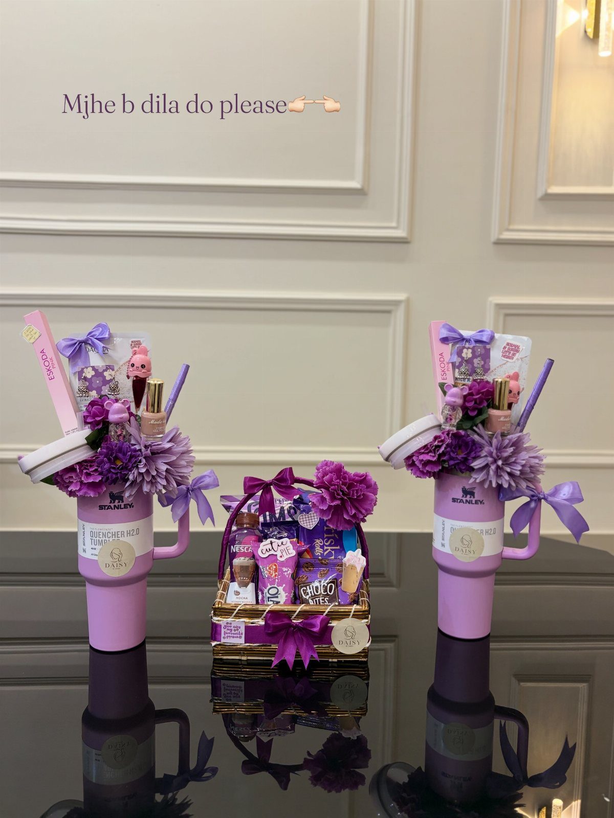 Purple themed gift baskets with cosmetics and flowers on a reflective black table