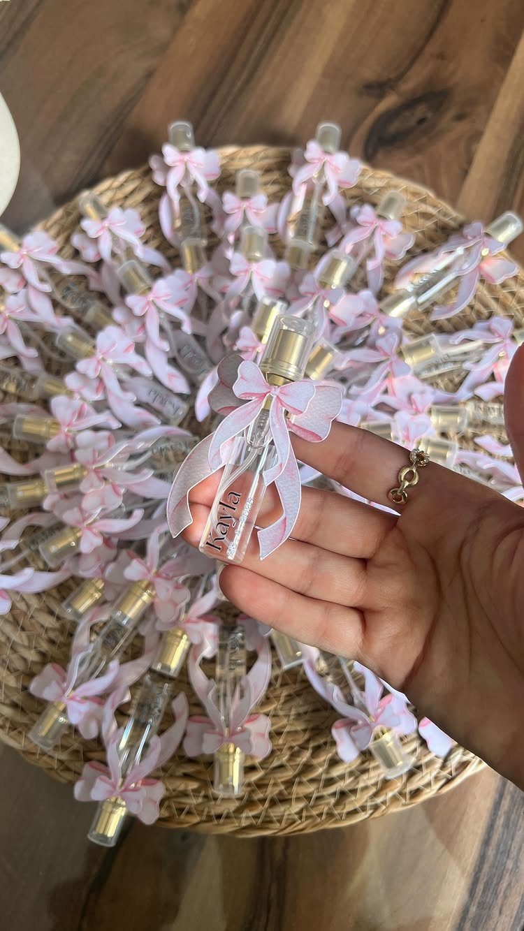 Small clear perfume bottles with pink ribbons arranged on a woven straw mat.