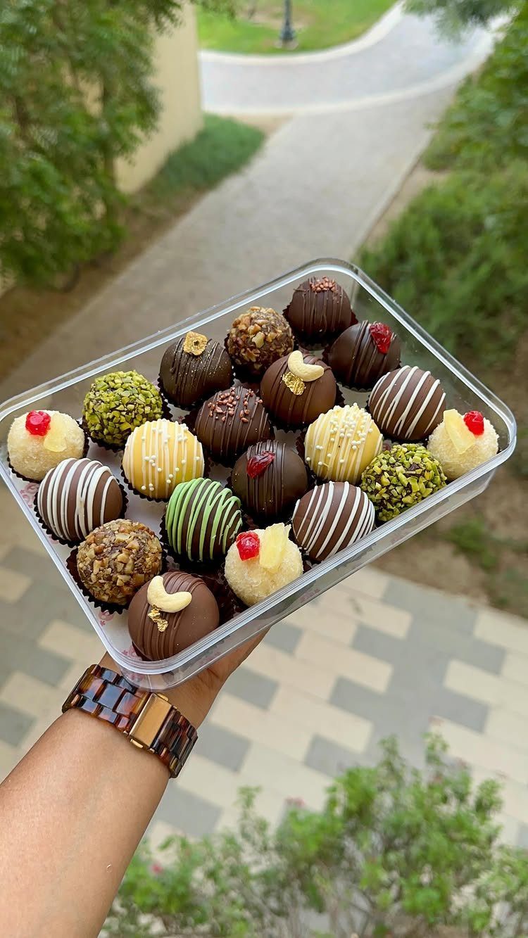 Assorted gourmet chocolate truffles in a clear plastic container held by a hand.