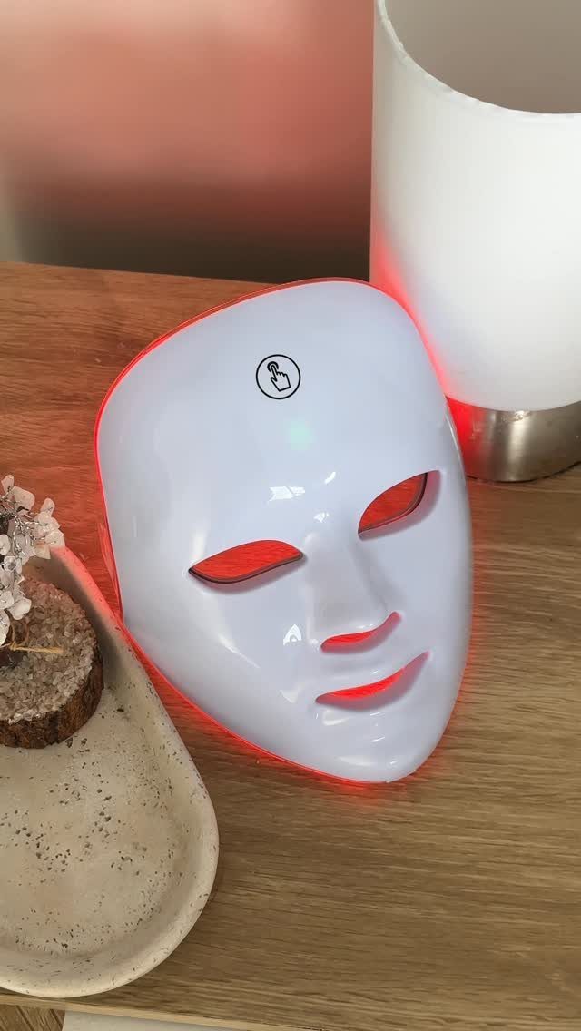 White LED light therapy face mask with red glow on a wooden table