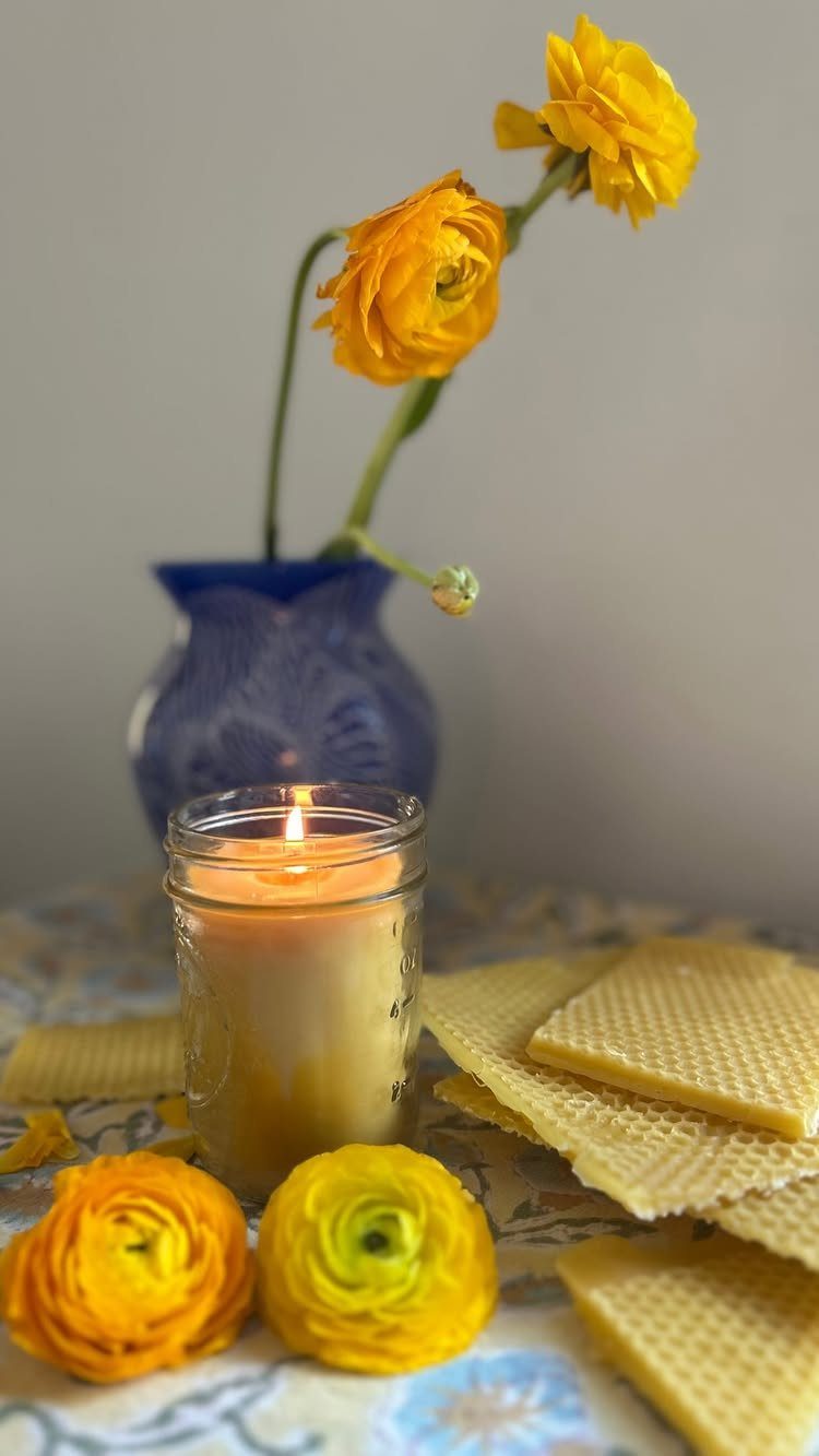 Lit candle in a mason jar with yellow flowers and honeycomb on a table