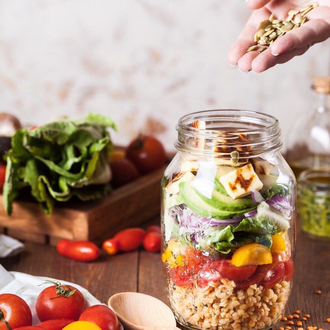 Layered salad in a mason jar with grains, vegetables, and tofu on wooden table