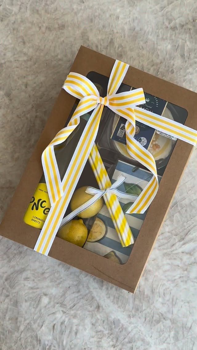 Gift box with yellow and white ribbon containing lemons and a yellow bottle.