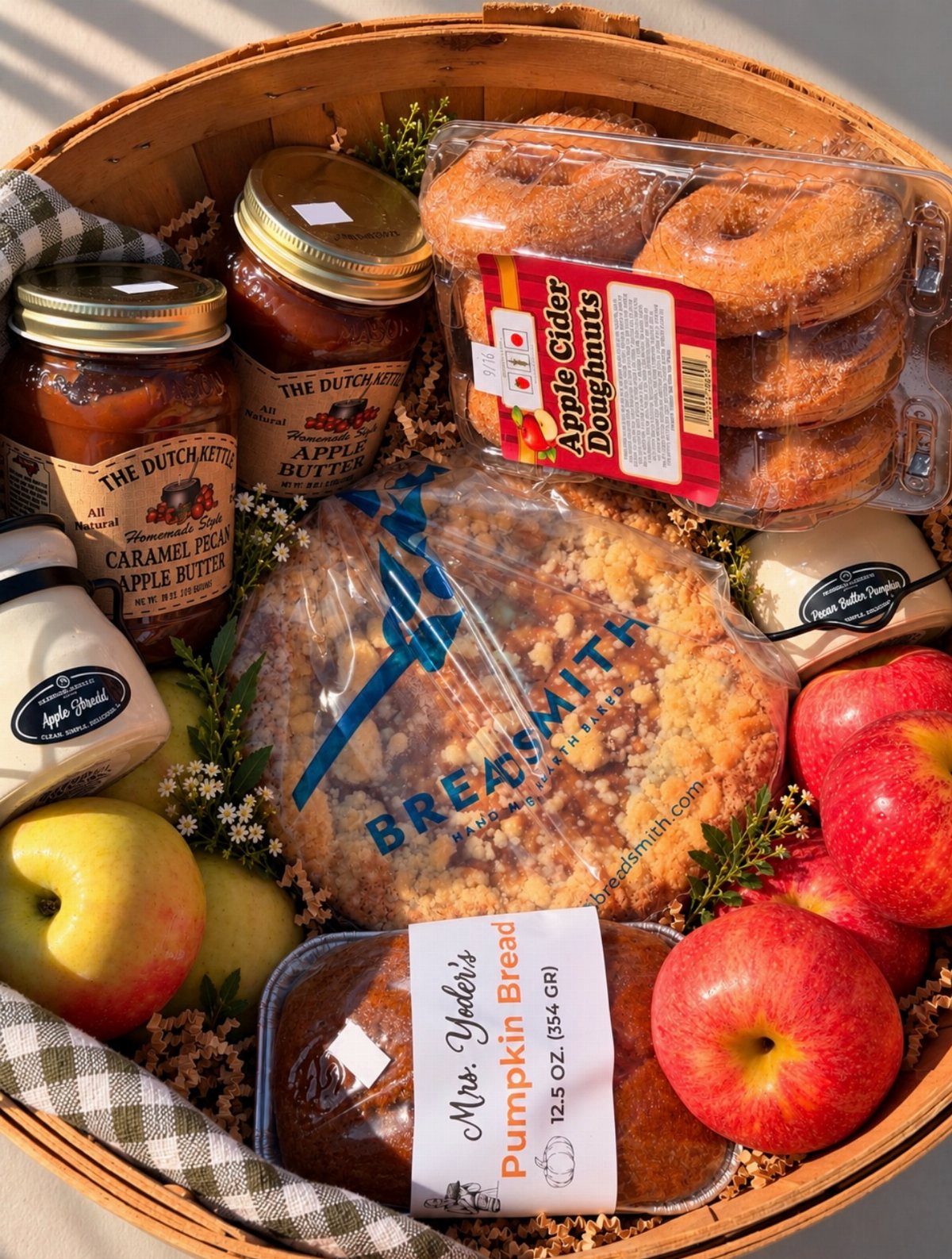 Wooden gift basket filled with apple butter, doughnuts, pumpkin bread, and red apples.