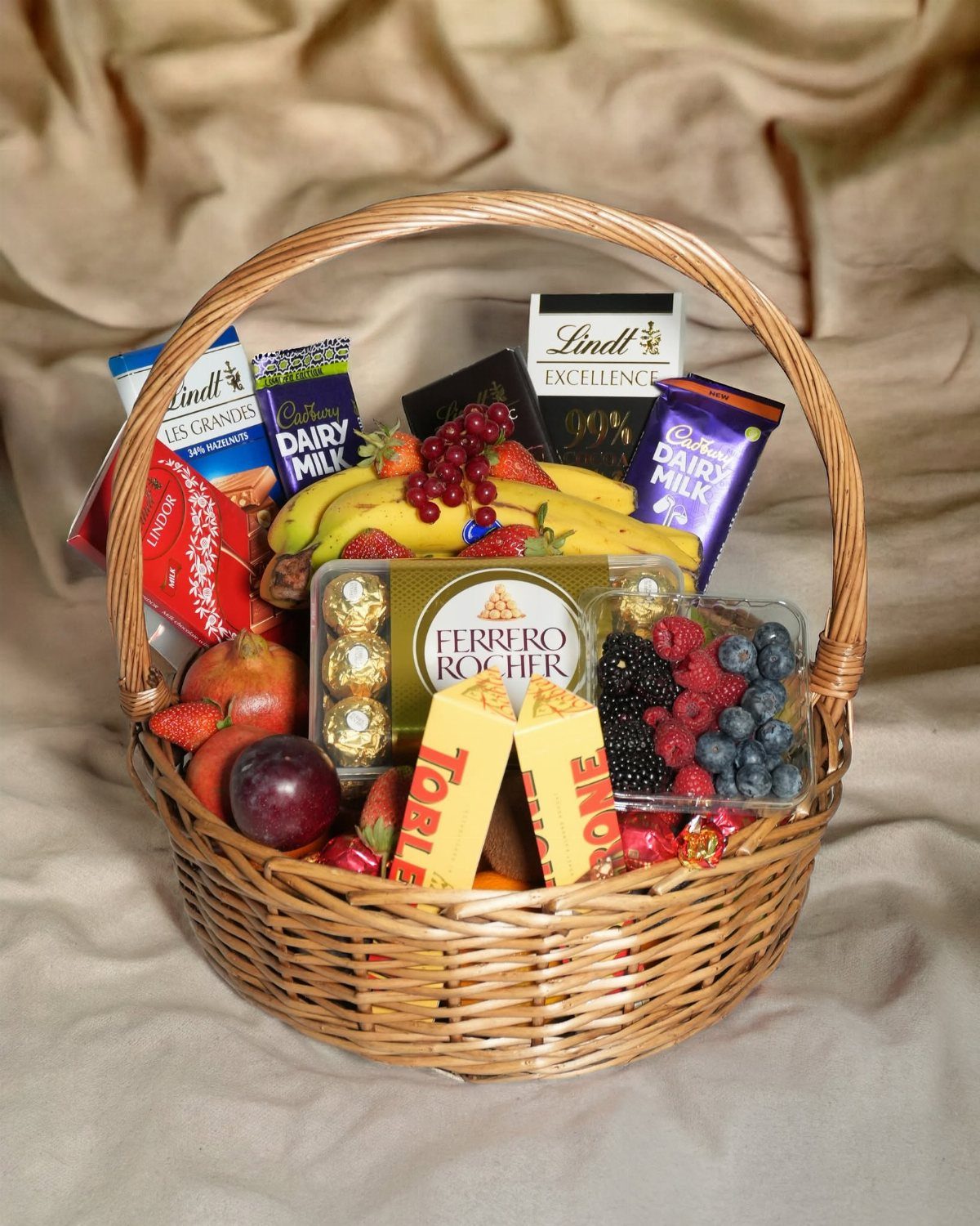 Wicker gift basket containing assorted chocolate bars and a variety of fresh fruits.