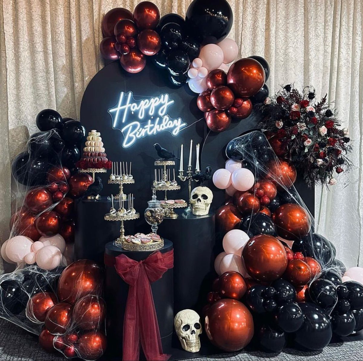 Birthday party setup with red and black balloons, skulls, and neon sign.