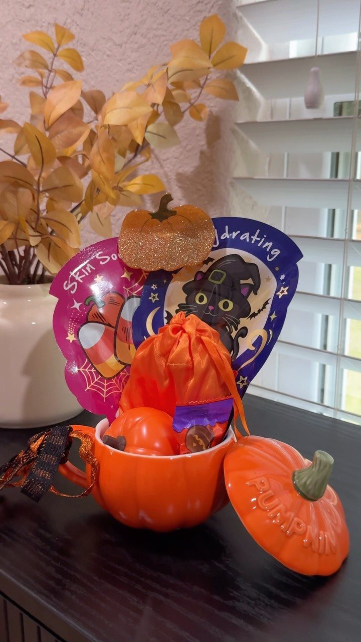 Pumpkin-shaped bowl filled with Halloween treats, a small pumpkin, and themed cards.