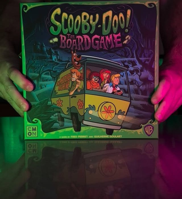 Scooby-Doo board game box held by hands under colorful neon lighting