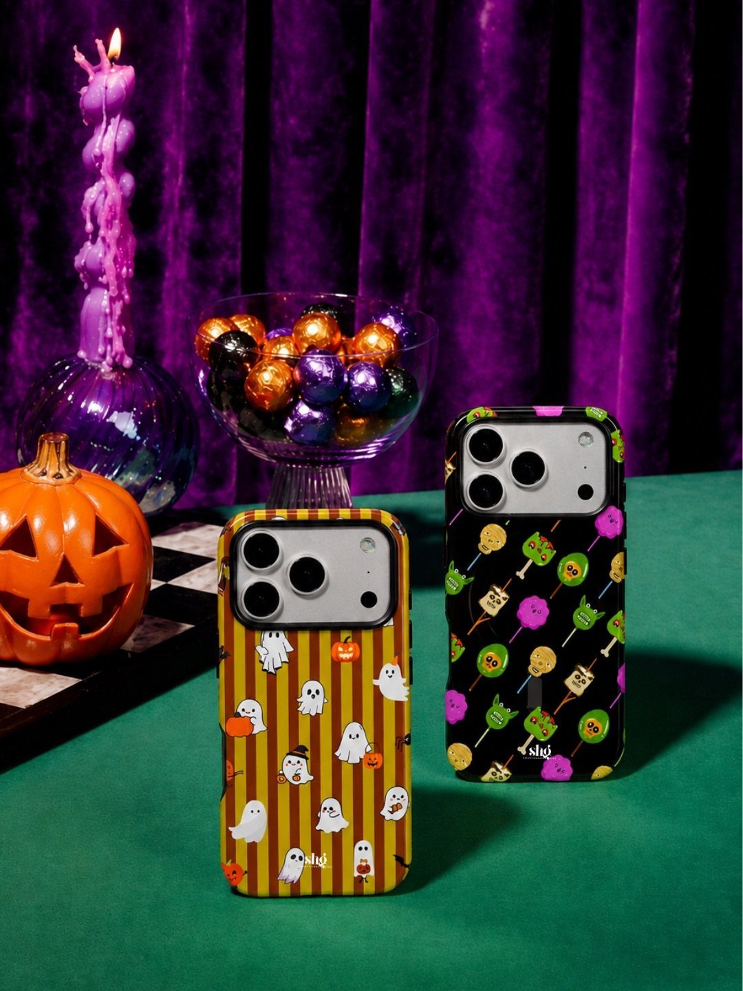 Two smartphones with Halloween-themed cases next to a pumpkin and candy bowl.