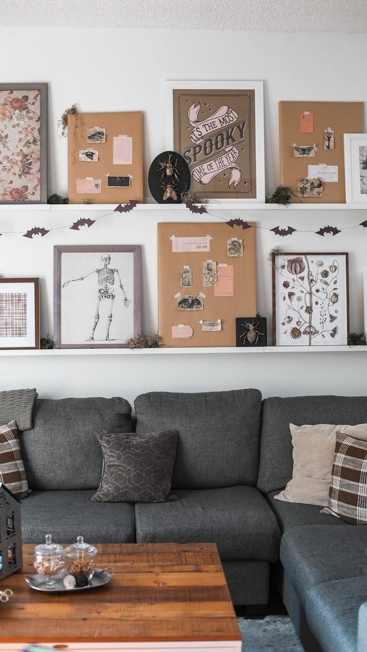 Spooky framed prints and mood boards displayed on white shelves above a grey sofa.