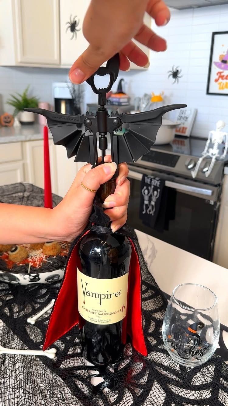 Bat-shaped wine stopper being placed in a vampire-themed wine bottle with a cape