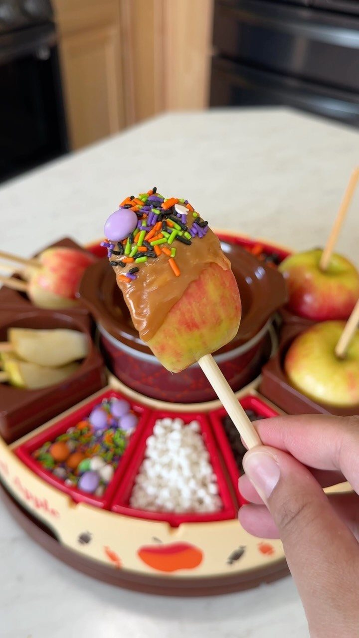 Halloween Food Gifts: 16 Sweet and Spooky Ideas 5 Caramel-dipped apple with colorful sprinkles held over a caramel apple dipping station.