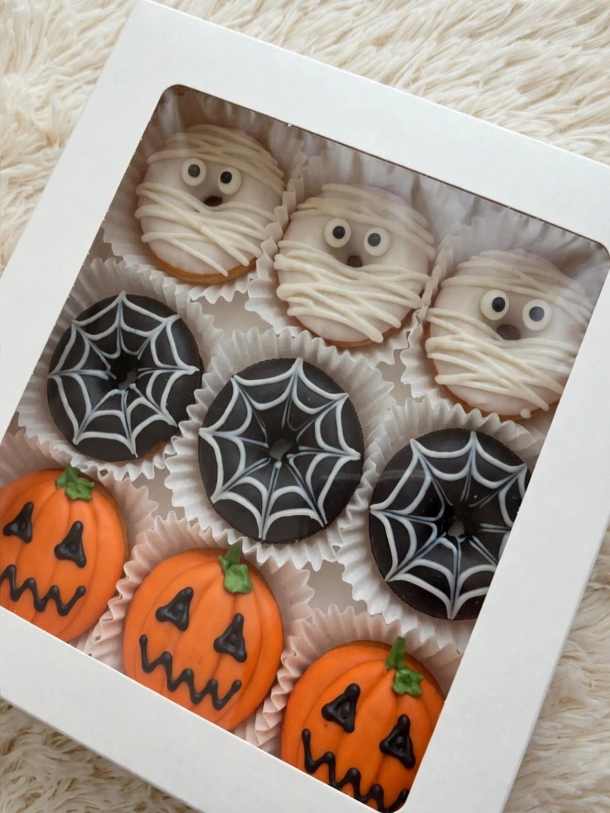 Halloween Food Gifts: 16 Sweet and Spooky Ideas 10 Halloween decorated donuts featuring mummies, spiderwebs, and pumpkins in a white gift box.