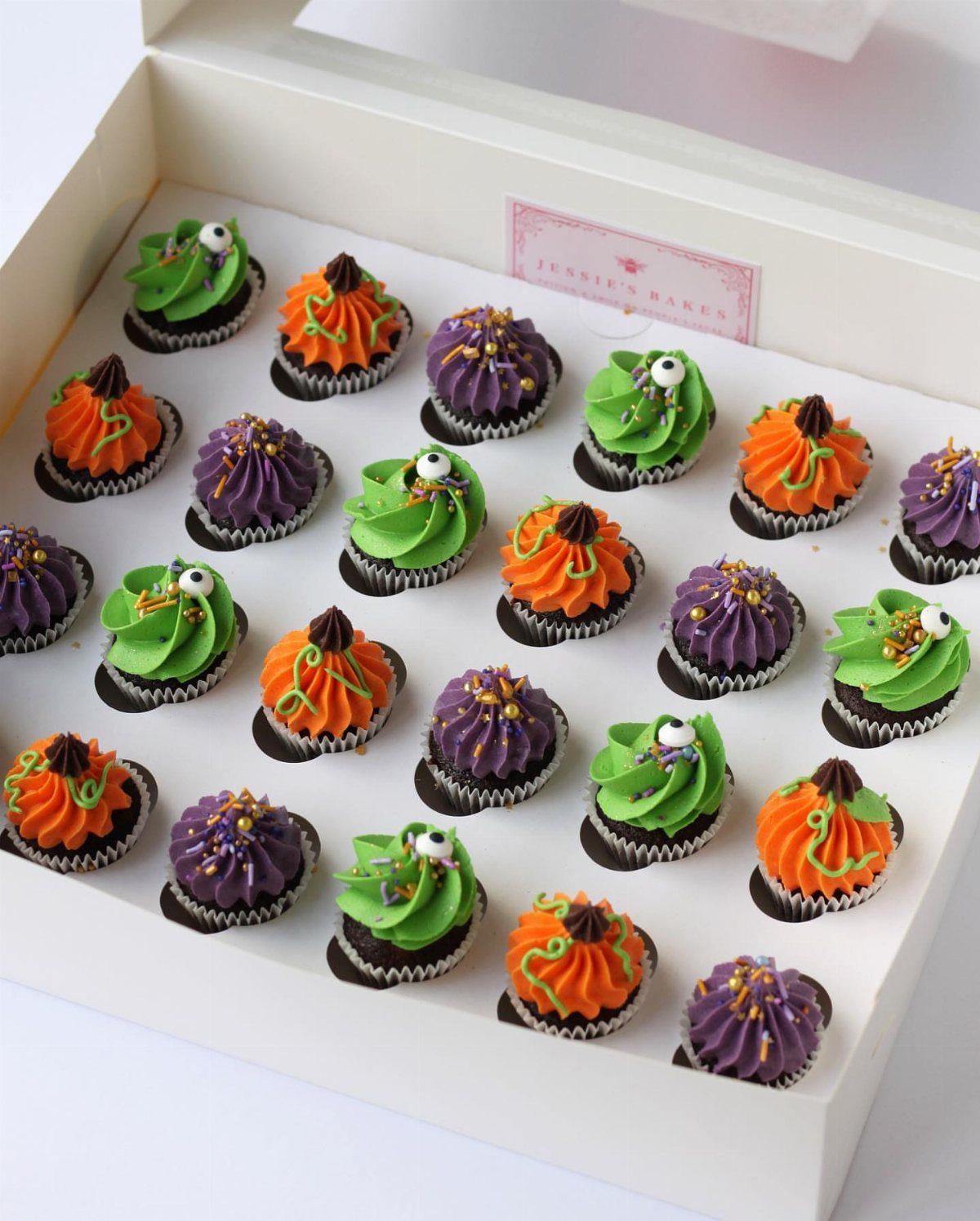 Halloween Food Gifts: 16 Sweet and Spooky Ideas 1 Mini chocolate cupcakes with green, orange, and purple frosting in a white box.
