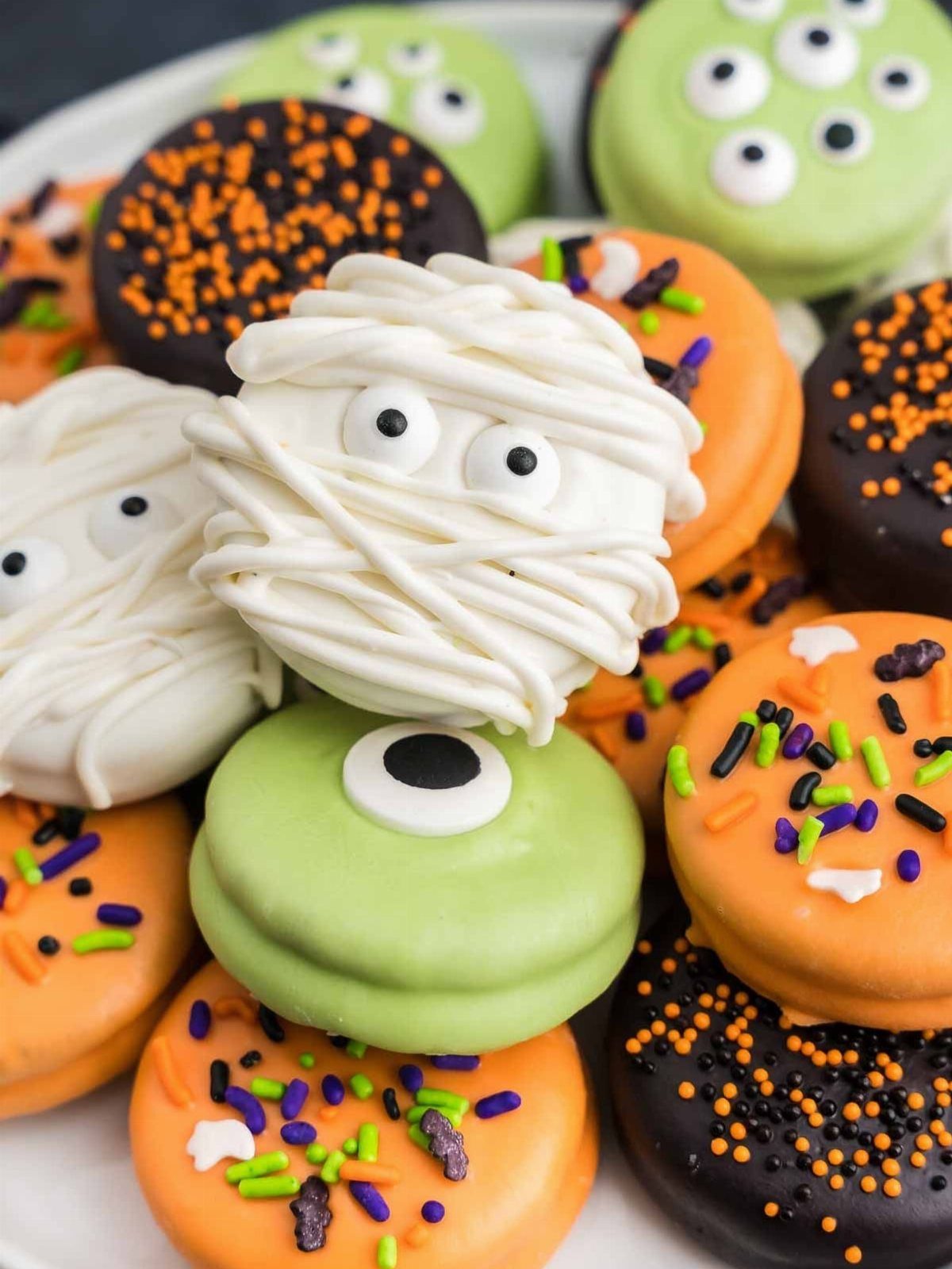 Halloween Food Gifts: 16 Sweet and Spooky Ideas 12 Halloween macarons decorated as mummies and eyeballs with orange and black sprinkles.