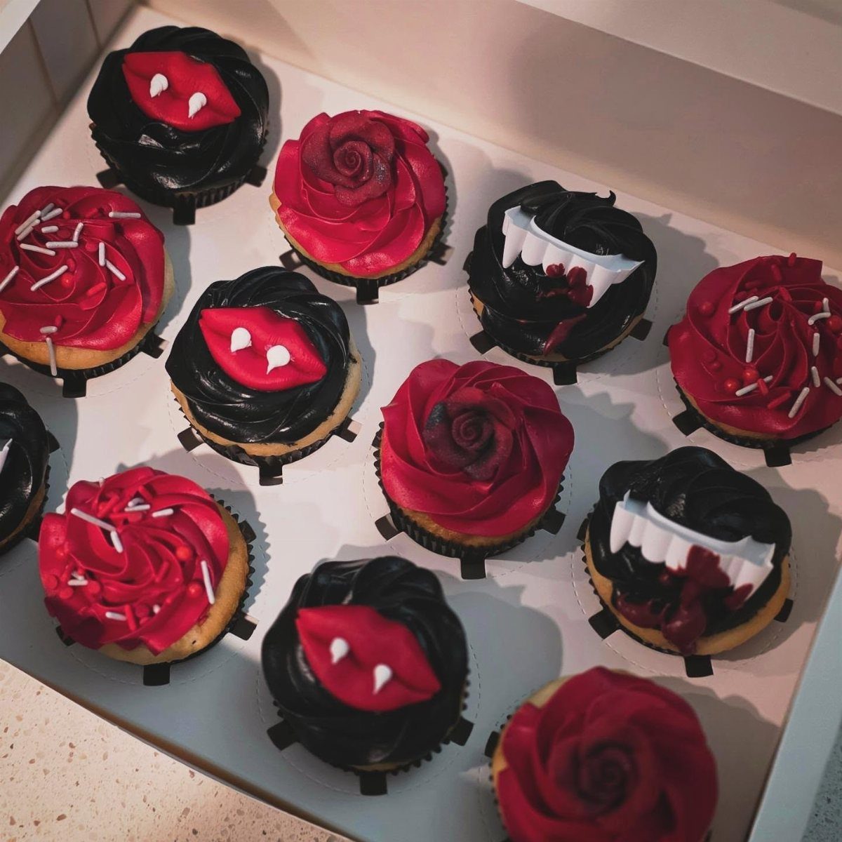 Halloween Food Gifts: 16 Sweet and Spooky Ideas 6 Assorted Halloween cupcakes with red roses and vampire fangs in a white box.