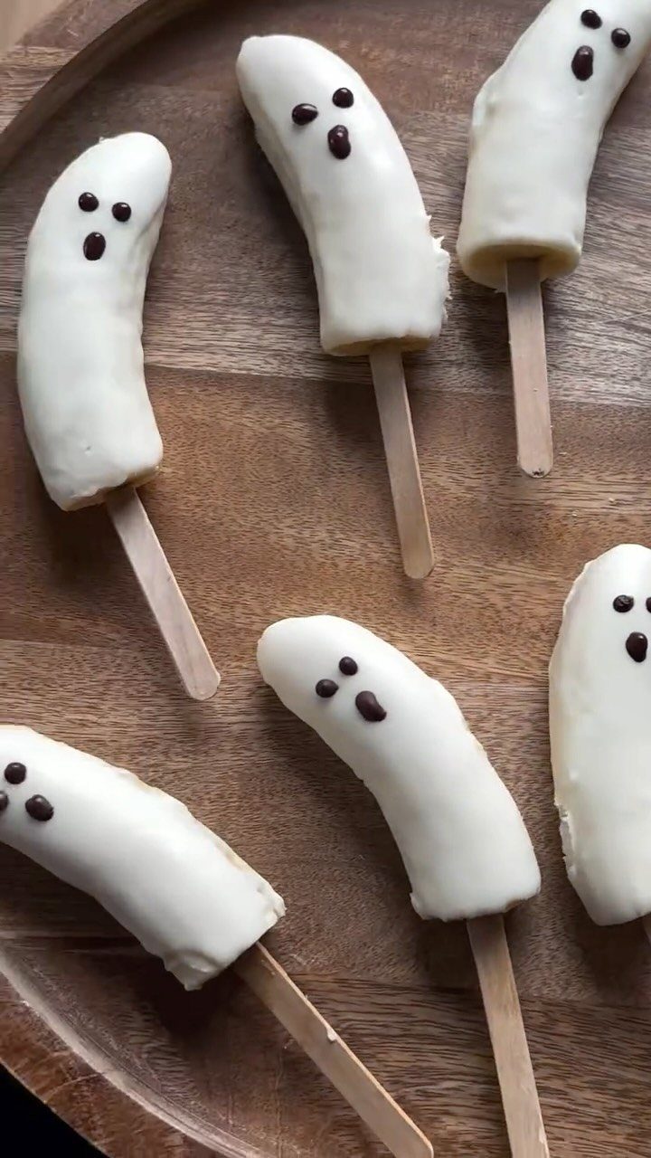 Halloween Food Gifts: 16 Sweet and Spooky Ideas 15 White chocolate covered banana ghost pops on a round wooden serving platter.