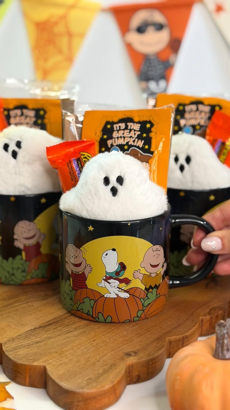 Peanuts themed Halloween mugs filled with plush ghosts and orange candy treats.