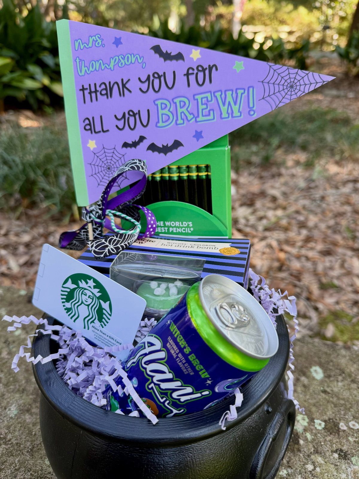 Black cauldron gift basket with purple filler, energy drink, and brew themed pennant.