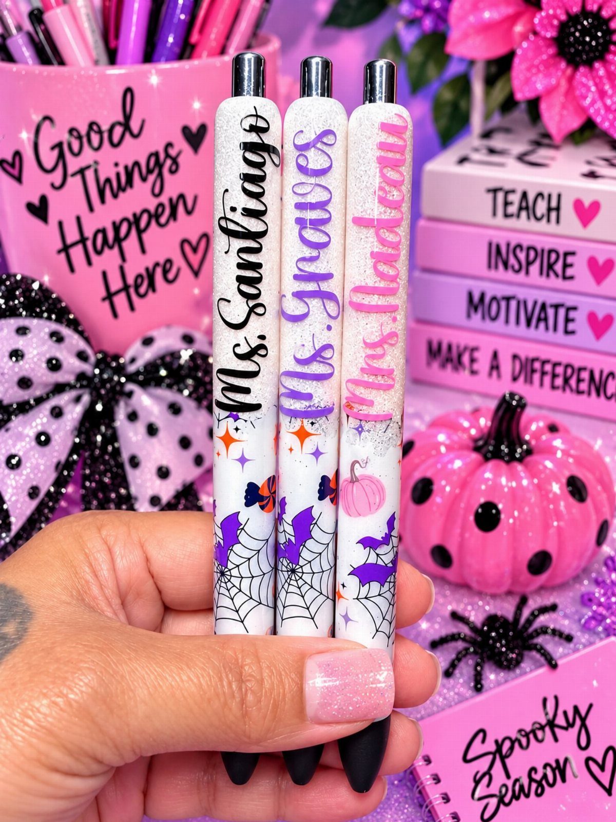 Halloween Teacher Gifts: 10 Ideas Teachers Will Like 6 Three personalized Halloween pens with spiderwebs and pumpkins held against a pink background.