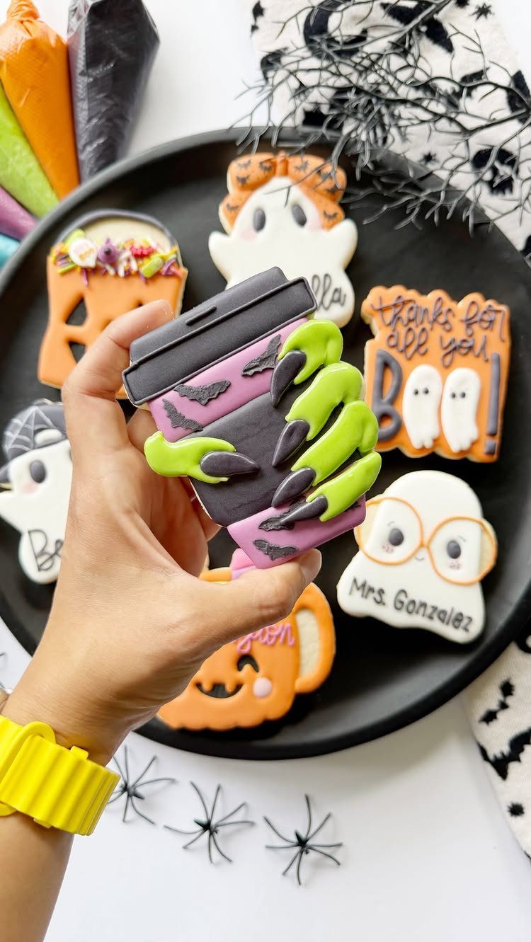 Halloween Teacher Gifts: 10 Ideas Teachers Will Like 5 Hand holding a Halloween treat over a plate of personalized ghost cookies.