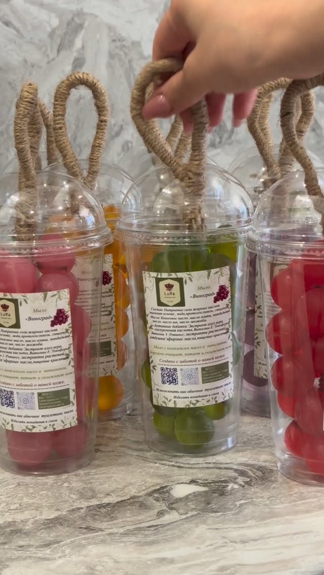 Bubble-shaped soaps in clear plastic cups with twine handles on marble surface