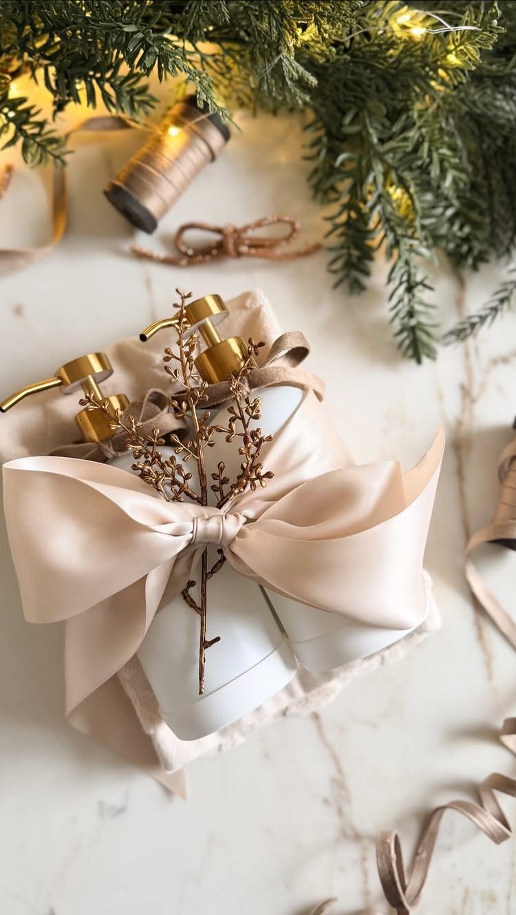 Two white soap dispensers with gold pumps wrapped in a champagne satin ribbon.