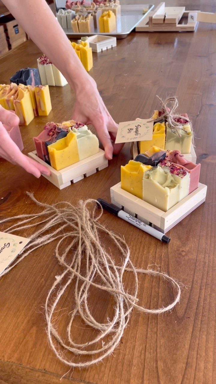Handmade colorful soap bars arranged in small wooden gift boxes on a table.