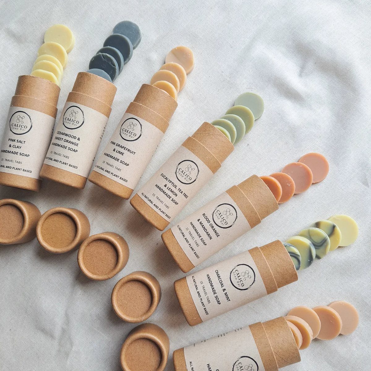 Small round soap discs stacked in cardboard tubes on a white fabric background.