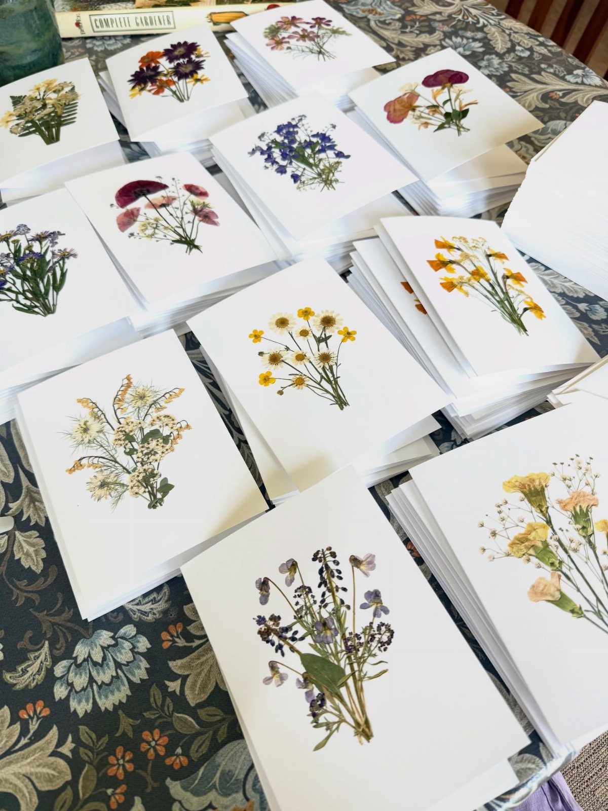 13 Homemade Gift Ideas for Coworkers They'll Use 8 White notecards featuring various colorful pressed dried flowers on a floral tablecloth.