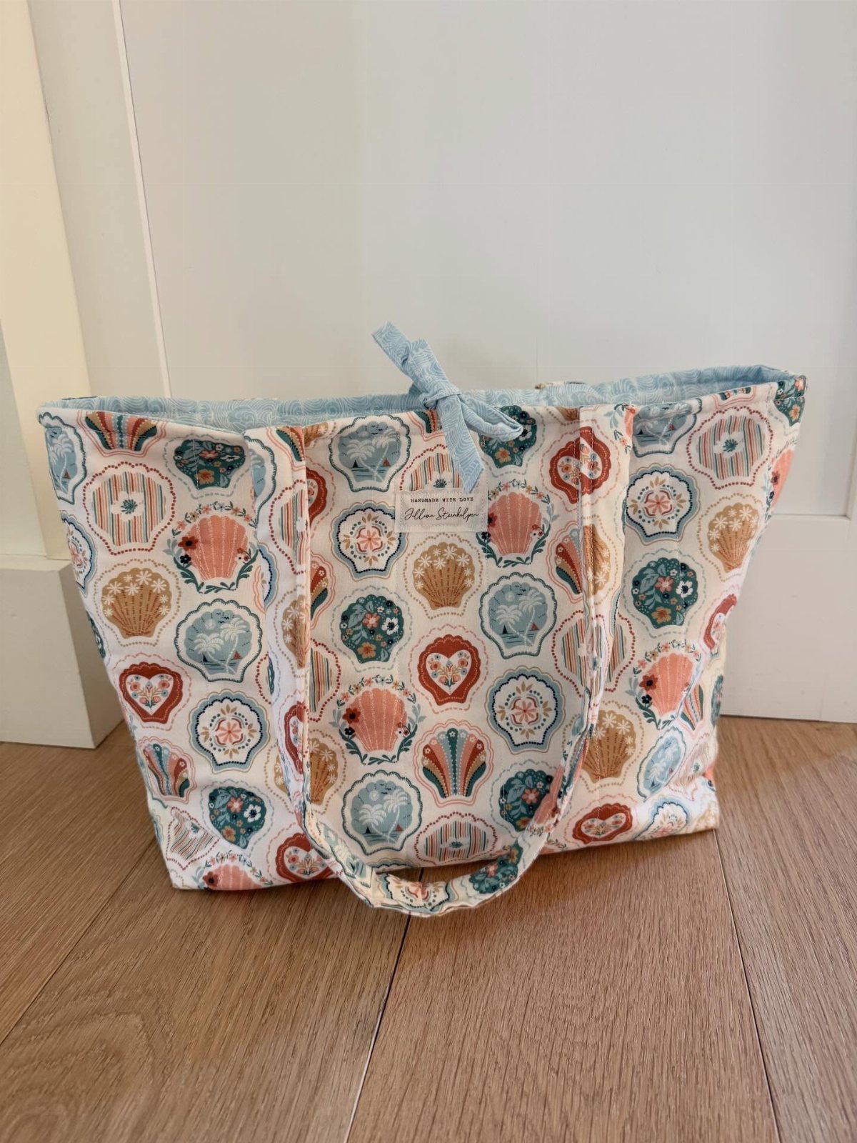 13 Homemade Gift Ideas for Coworkers They'll Use 9 Fabric tote bag with colorful shell patterns sitting on a wooden floor.