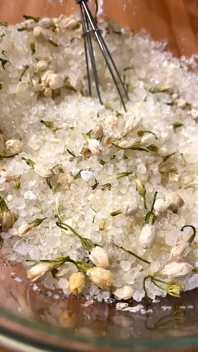 White bath salts mixed with dried jasmine buds in a glass jar