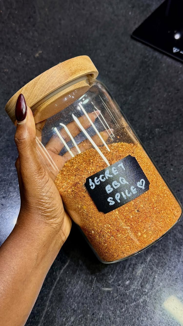 Glass jar filled with orange-brown BBQ spice seasoning held by a hand.