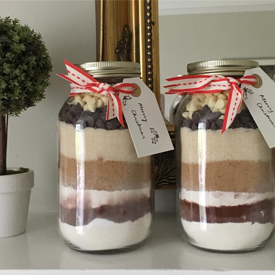 Two glass jars with layered brownie mix, red ribbons, and Christmas gift tags.