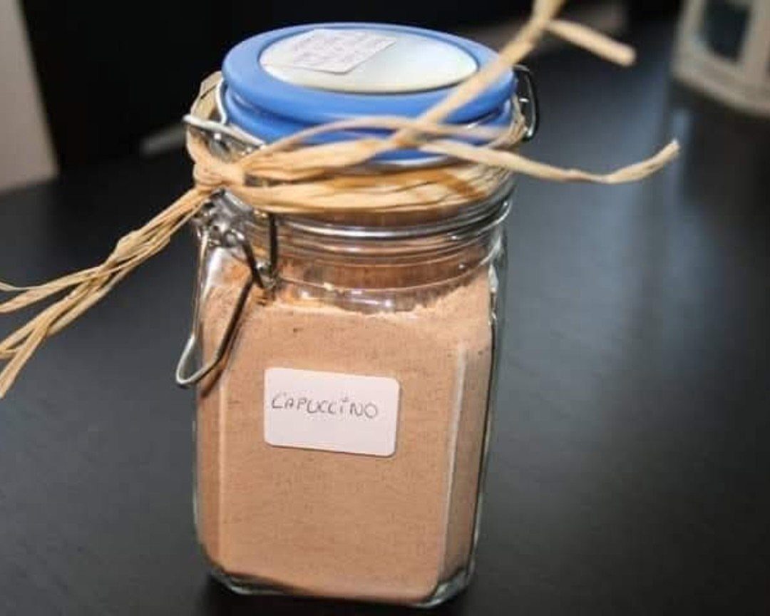 Glass jar filled with cappuccino mix powder, tied with raffia and labeled.