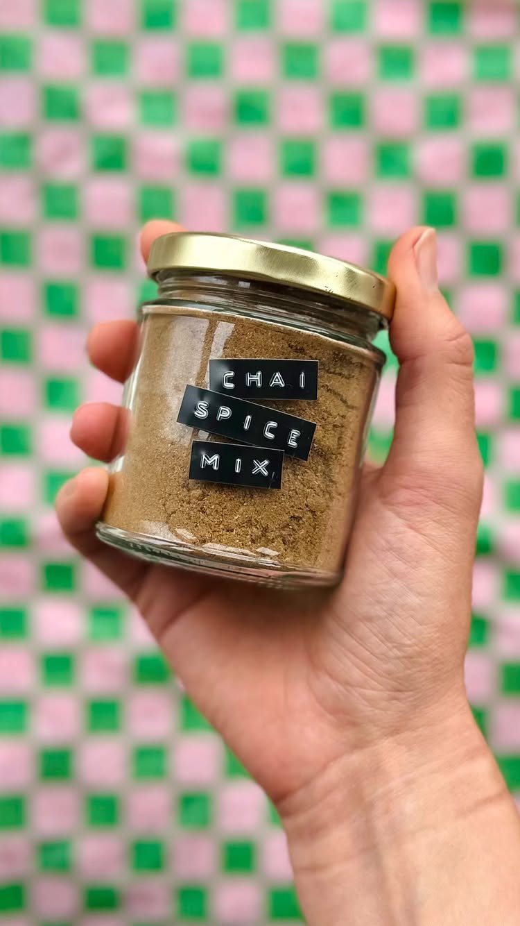 Hand holding a glass jar of chai spice mix against a checkered background.