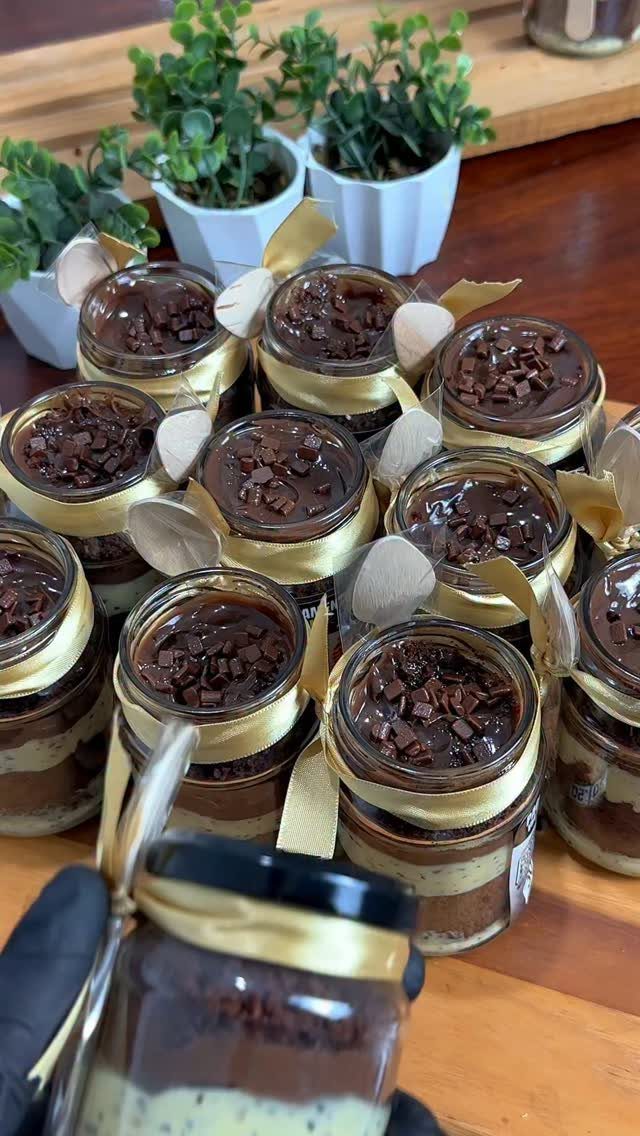 Layered chocolate cream pie desserts in small glass jars tied with gold ribbons.
