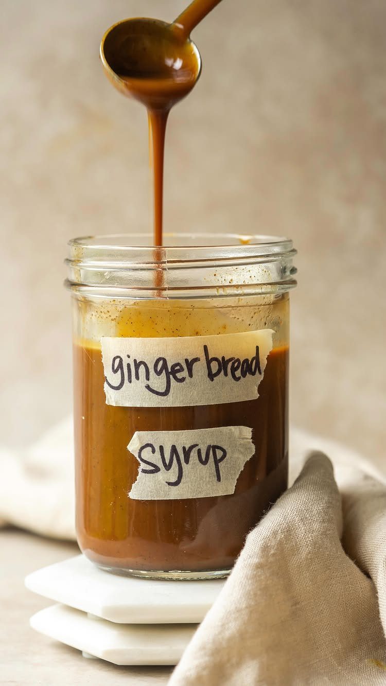 Gingerbread syrup being poured from a spoon into a labeled glass jar.