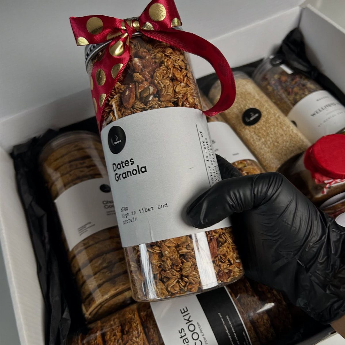Glass jar of dates granola with a red polka-dot ribbon in a gift box