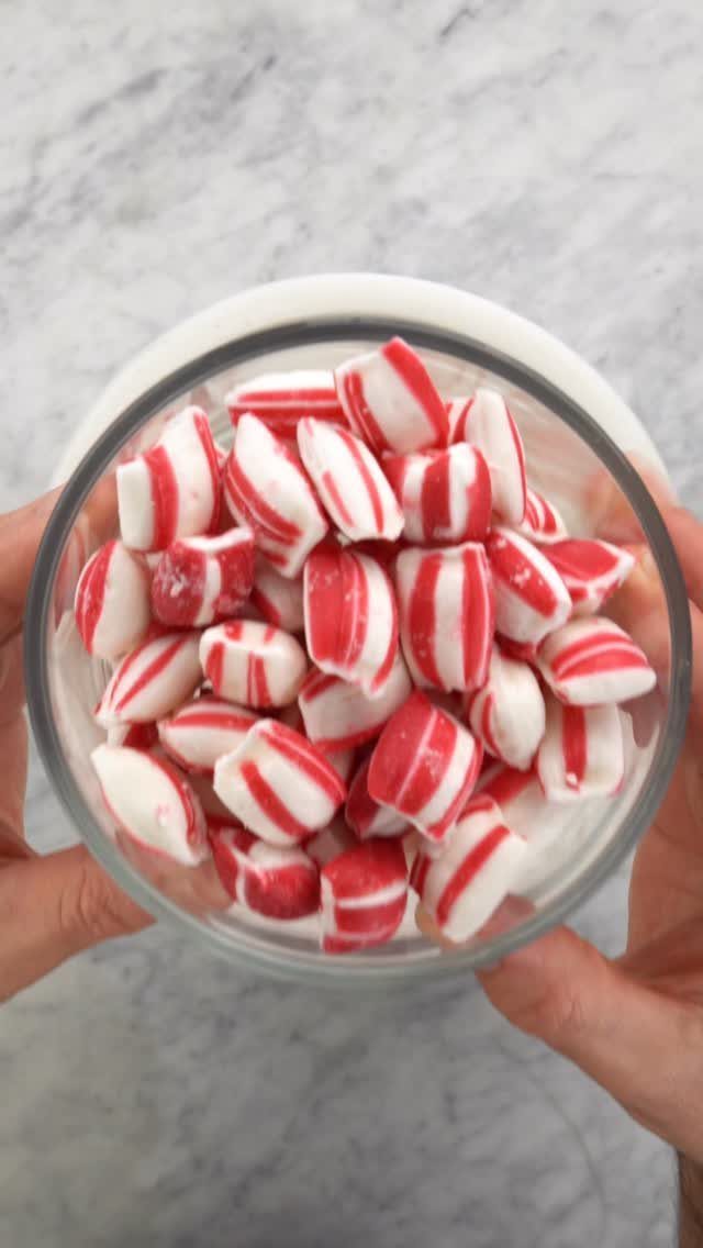 Hands holding a glass jar filled with red and white peppermint candies.