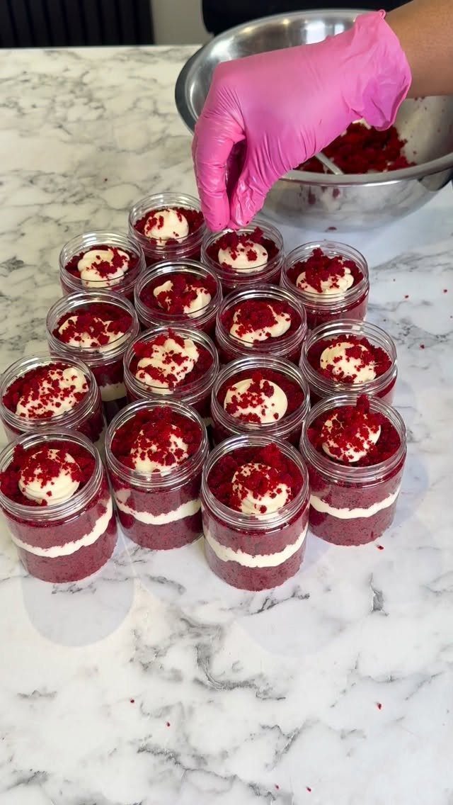 Layered red velvet cake jars with white cream on a marble countertop.