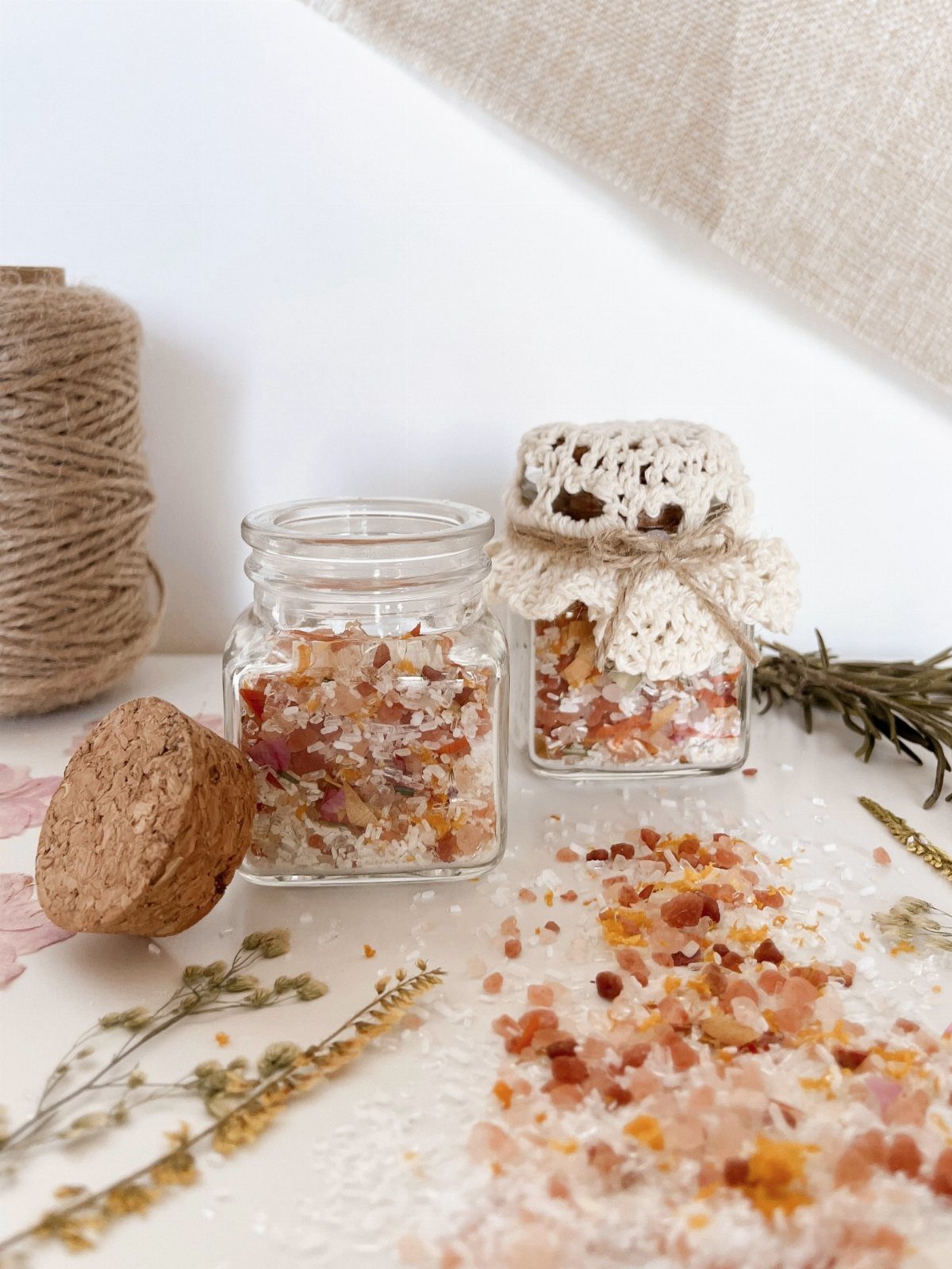 Glass jars filled with orange and pink bath salts and dried botanicals.