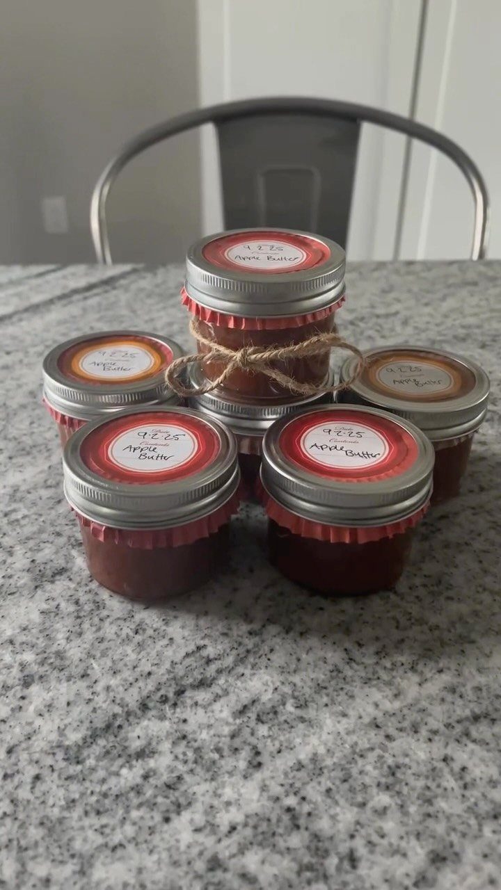 Six mason jars of apple butter with red fabric and twine bows.