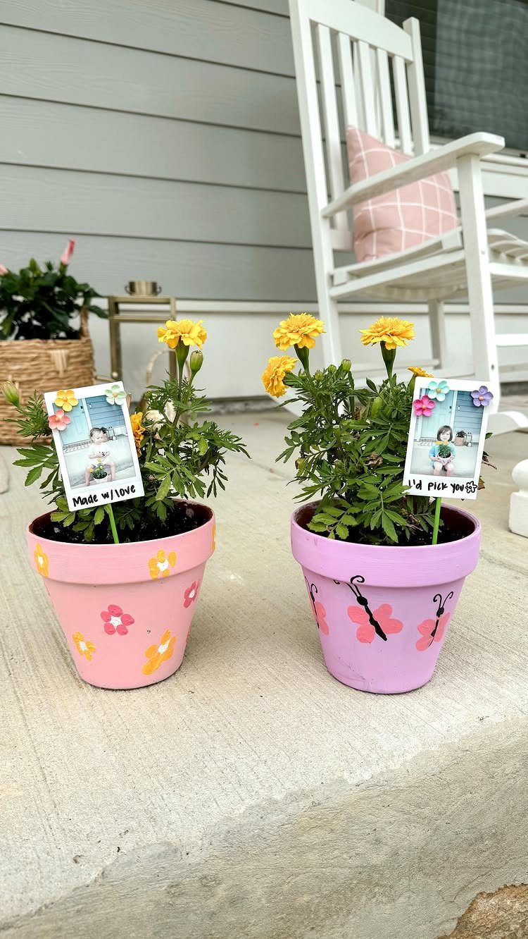 Two painted flower pots with yellow marigolds and personalized photo messages on a porch.