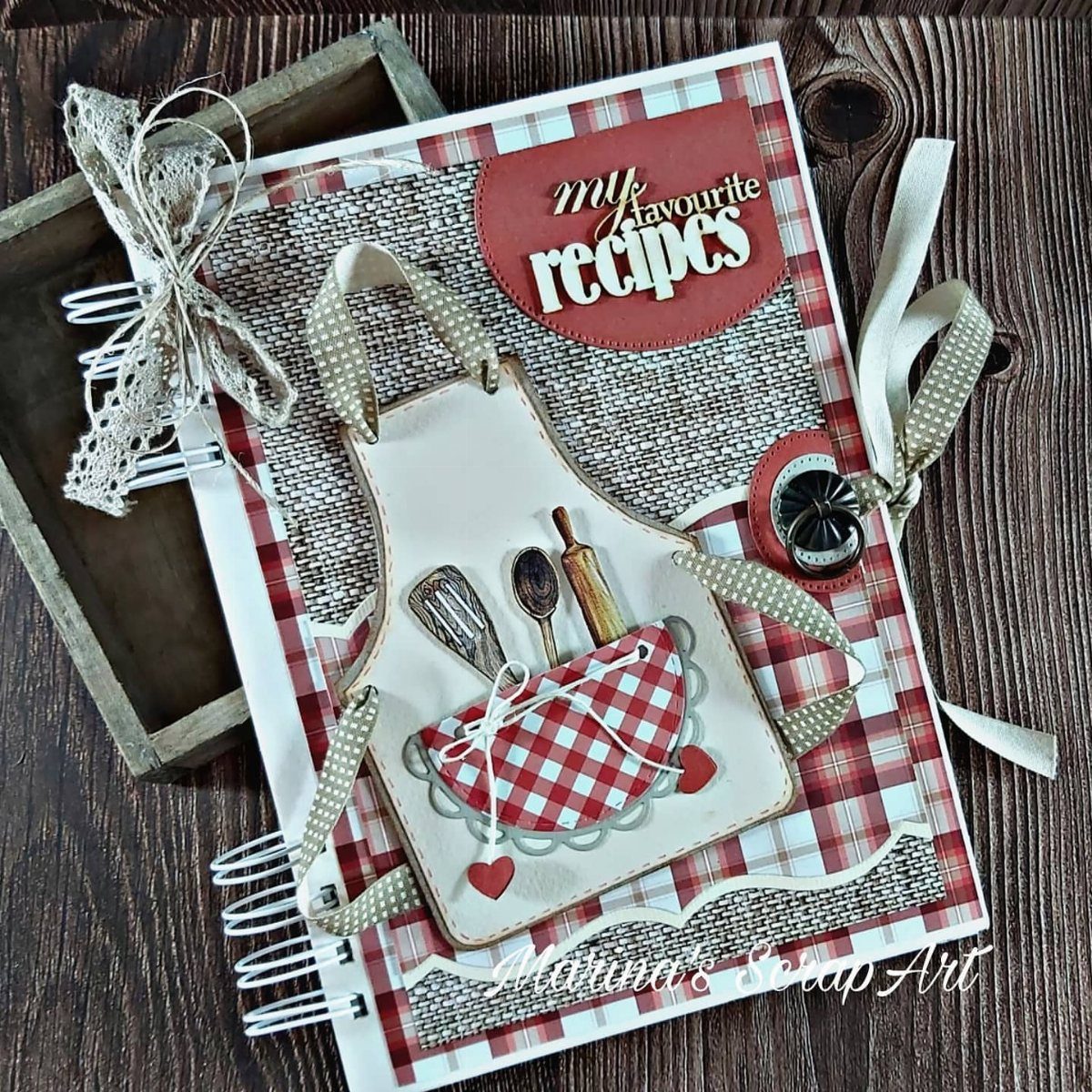 Handmade recipe book with a 3D apron and miniature kitchen utensils on wood.