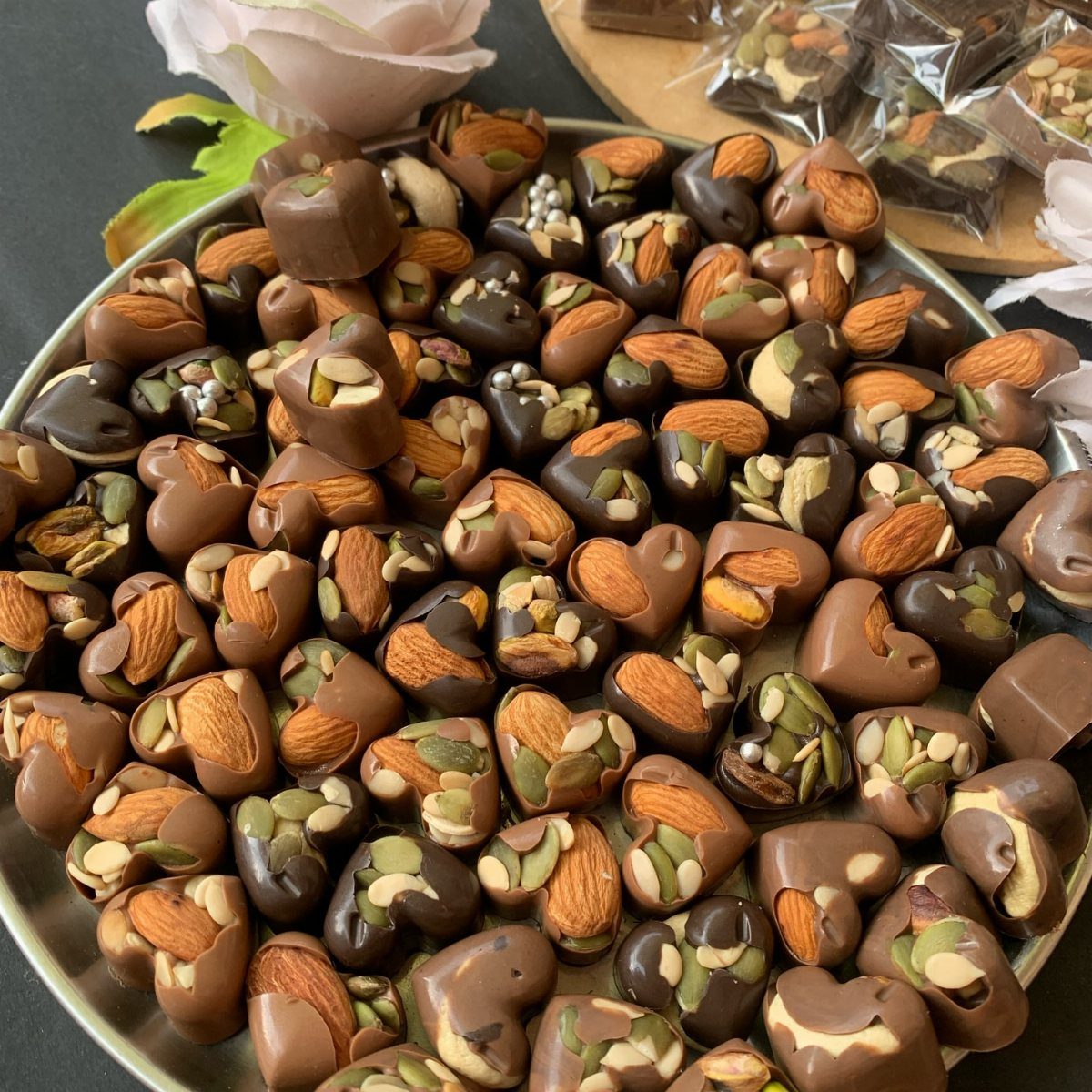 Heart-shaped chocolates topped with almonds and seeds on a plate with a rose.