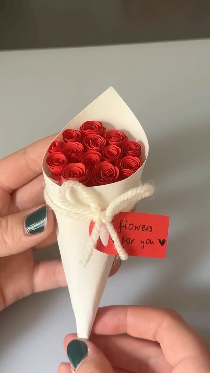 Small bouquet of red paper roses in a white cone wrap with twine.