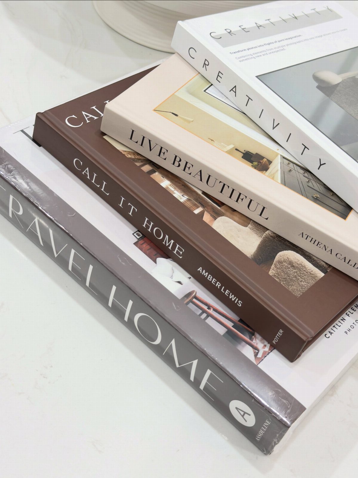 5 Housewarming Gift Ideas for Someone Who Has Everything 3 Stack of stylish hardcover coffee table books on a white marble surface.