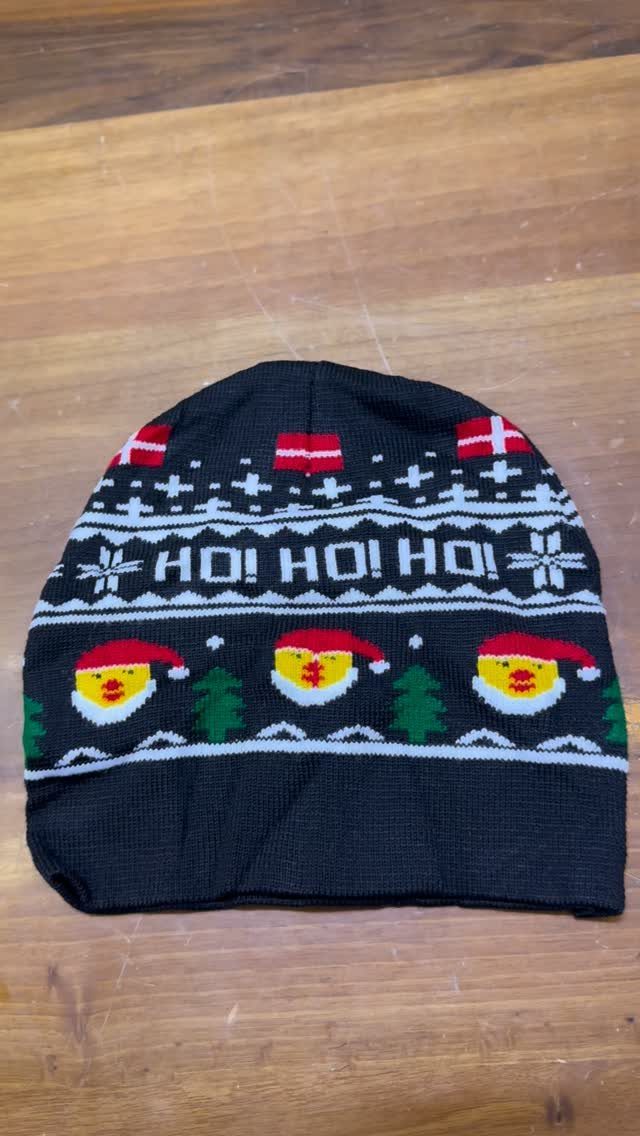 Black knit Christmas beanie with Santa faces and HO HO HO text on wood.